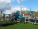 Crash scene showing a damaged blue truck after a collision with a freight train near Waikanae Railway Station, with emergency workers on site and road signs pointing to Elizabeth Street and Kāpiti Coast Museum.